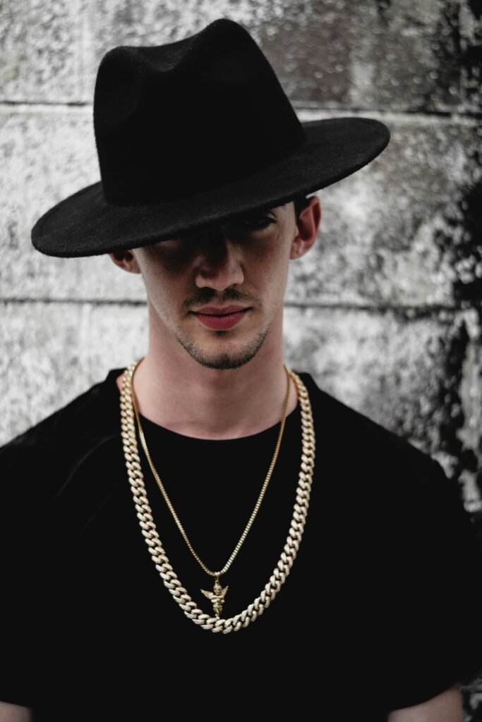 Portrait of a fashionable man wearing a black hat and gold chains against a textured background.